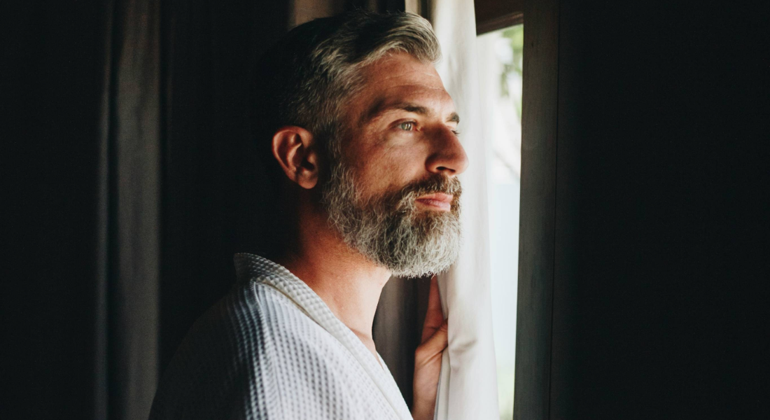 Man with beard looking out of a window